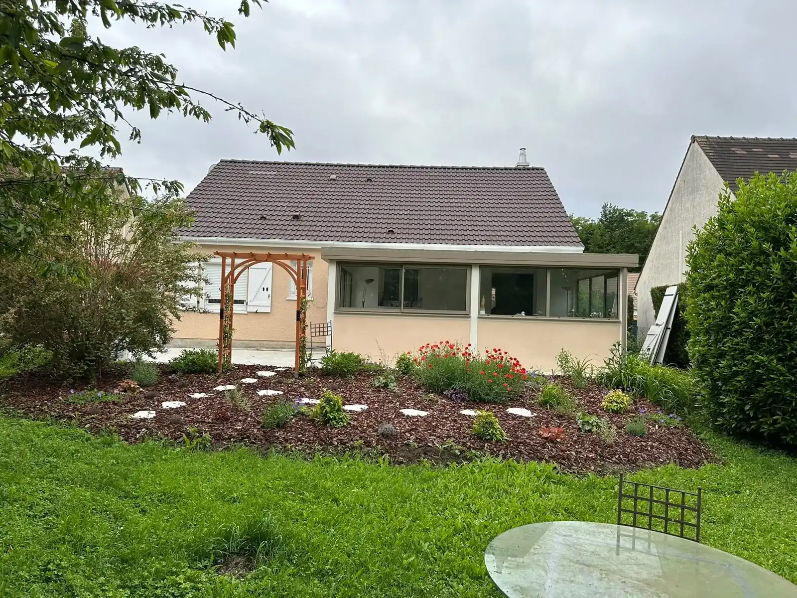 Extension de plain-pied avec pergola, ouverte sur un jardin fleuri