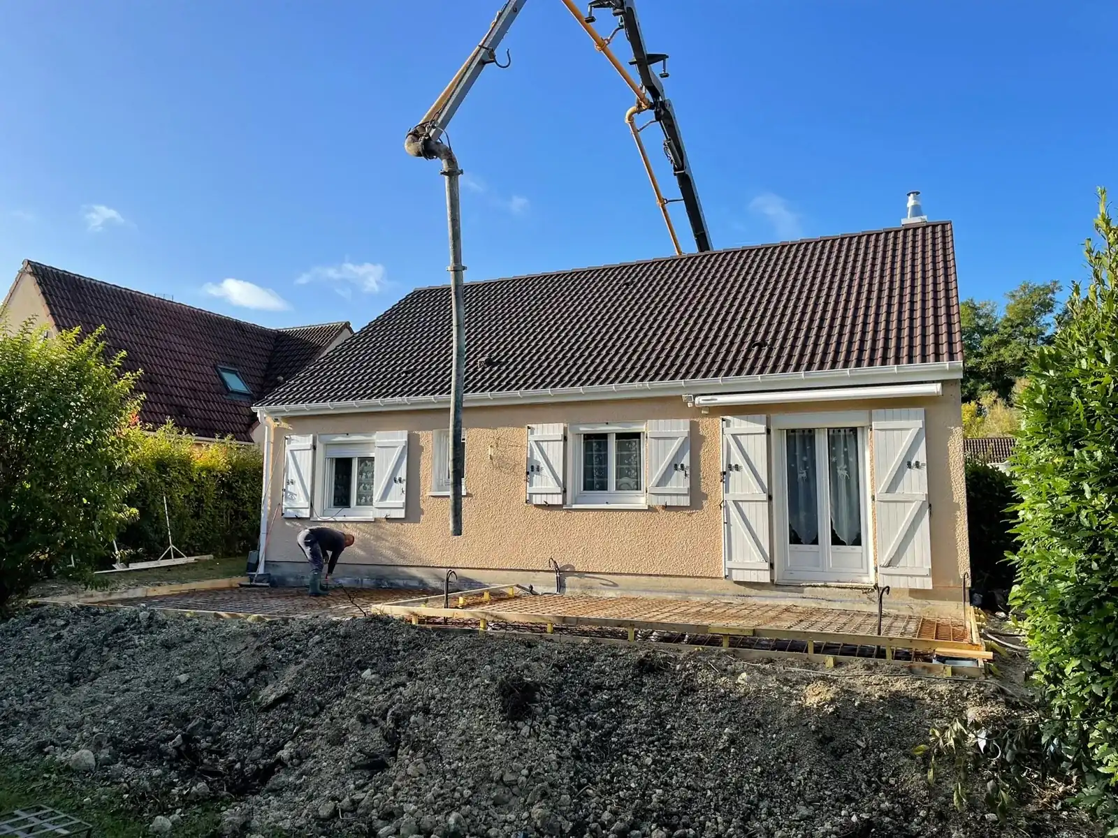 Un camion-pompe coule le béton, un maçon de l’équipe au pied du chantier