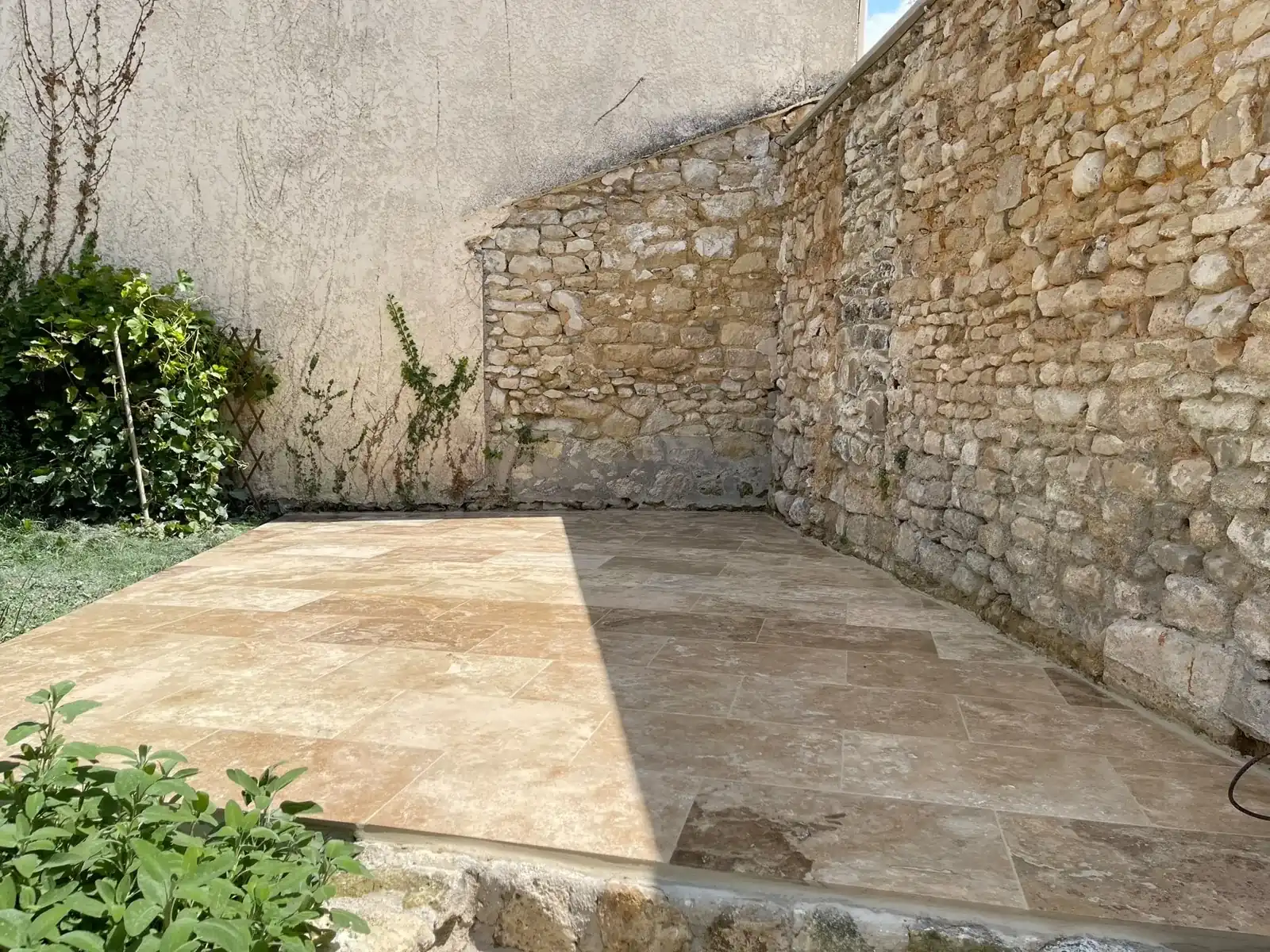 Terrasse en dalles de travertin au pied d’un mur en pierre
