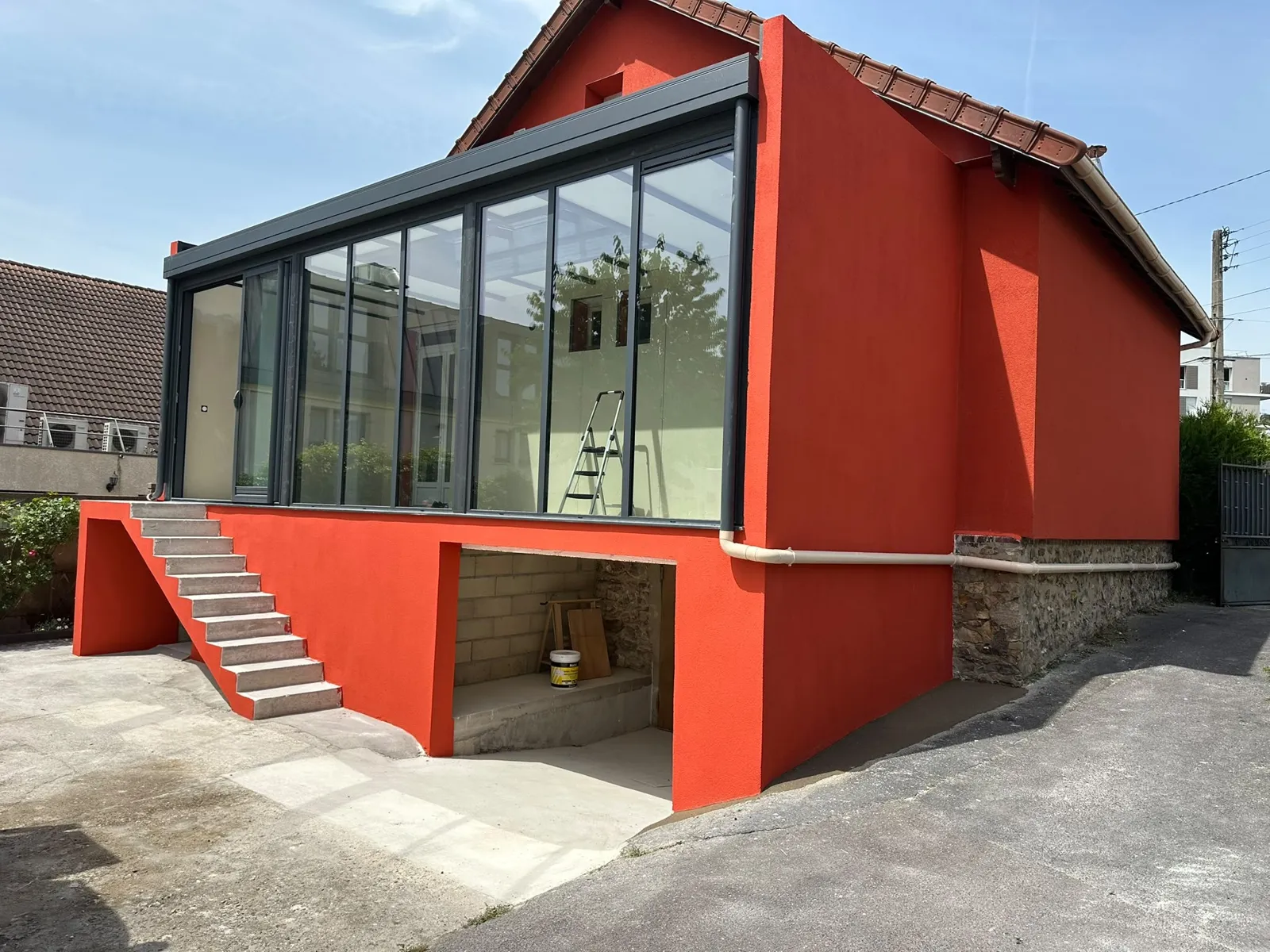 Véranda vitrée noire sur façade rouge, escalier maçonné